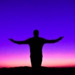 Silhouette of a person with outstretched arms against a vivid sunset sky.